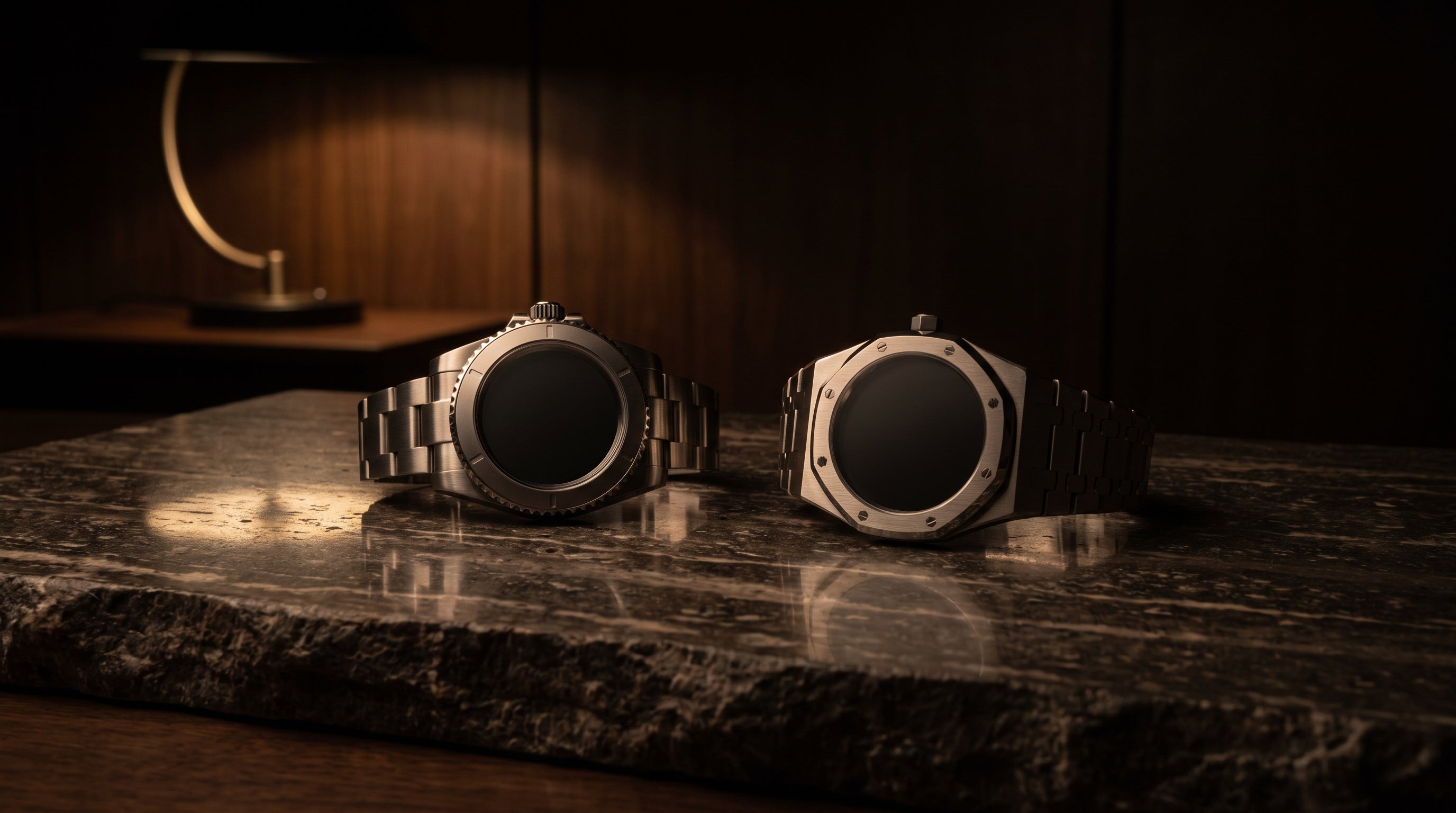 Two steel luxury sports watches side by side on dark travertine, one with a round bezel and one with an octagonal bezel and integrated bracelet, lit by warm low-key light.